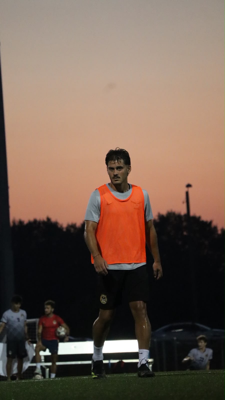 An NC United FC player in a training bib waiting on the field as the sky glows orange at dusk