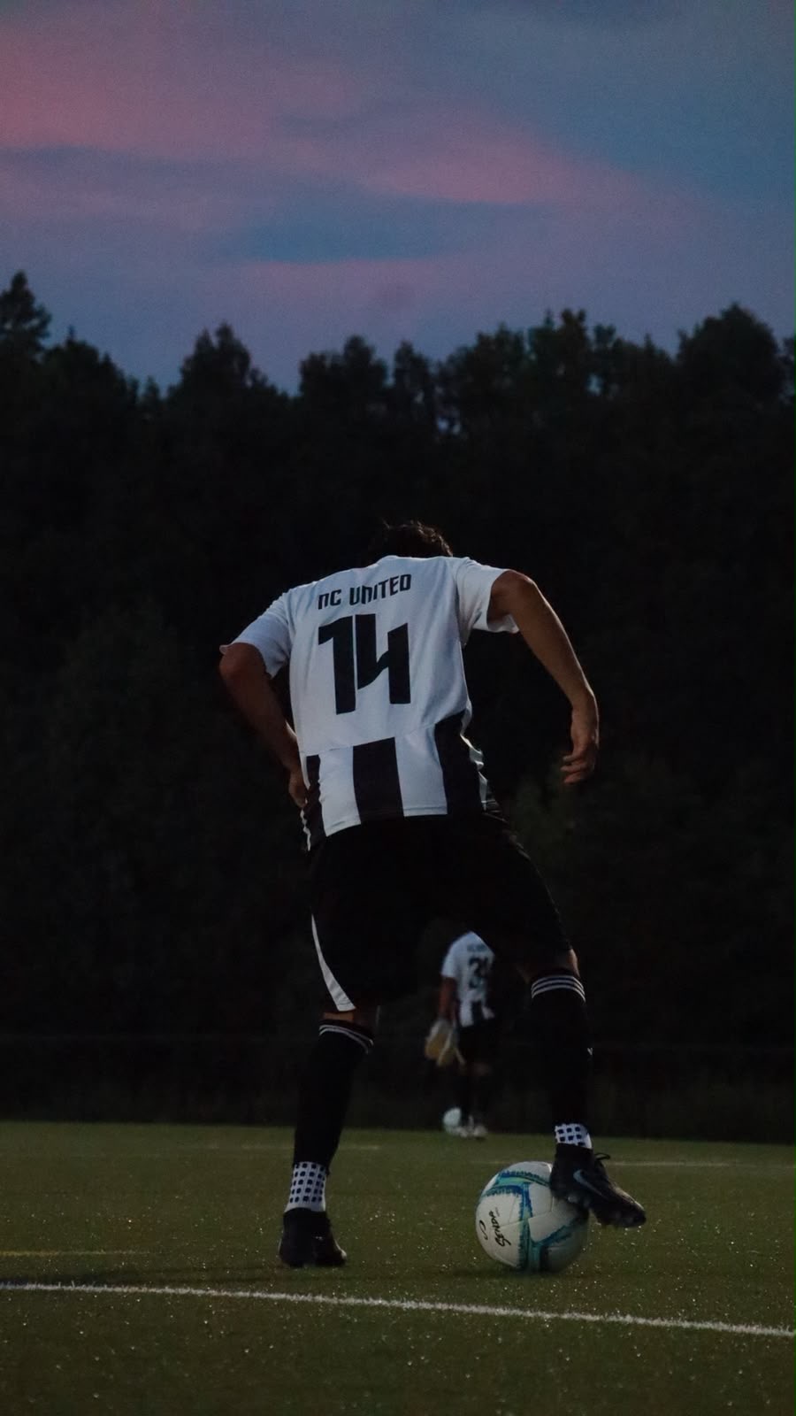 An NC United FC player wearing number 14 stepping onto the ball at dusk, seen from behind