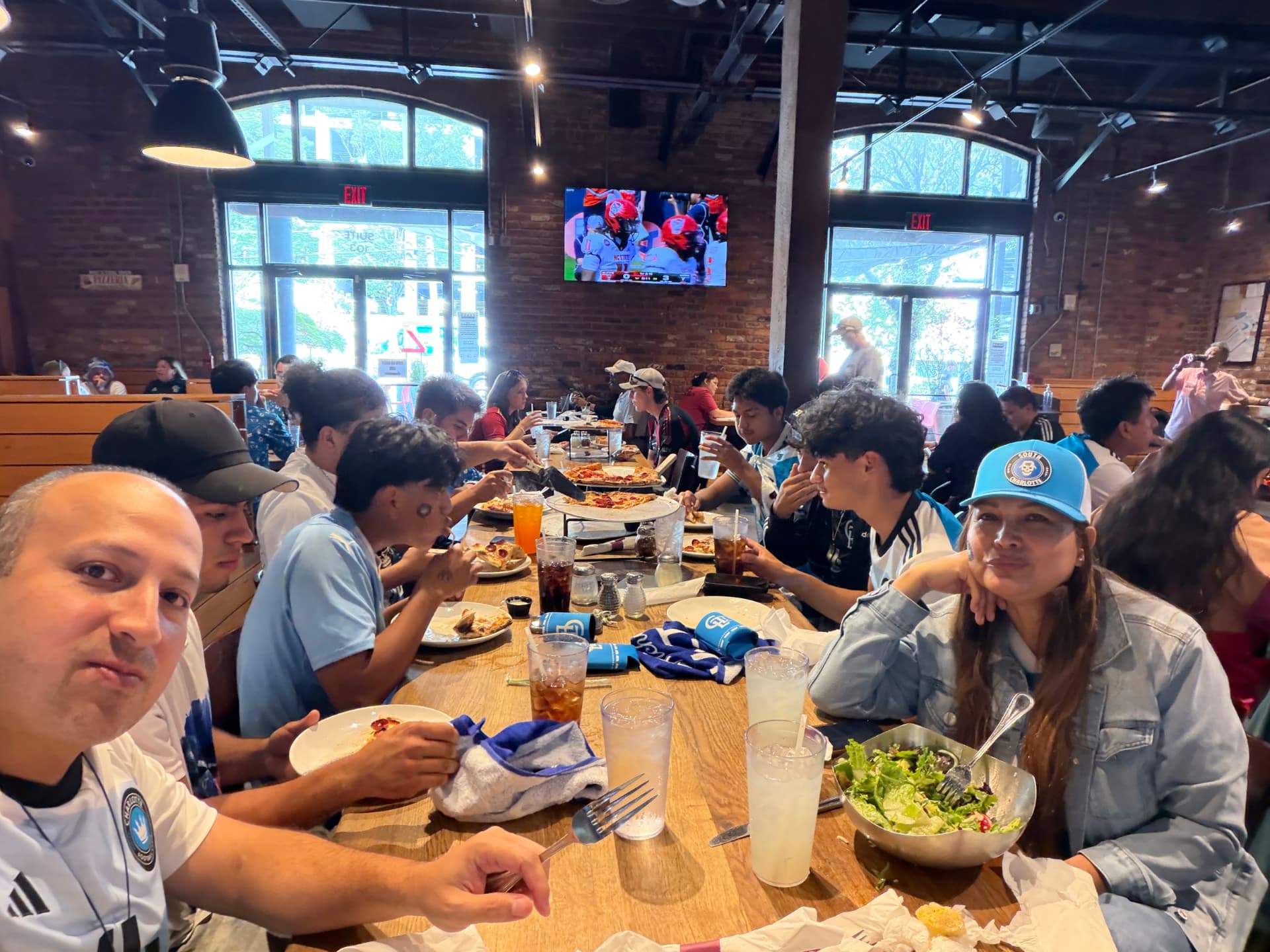 NC United FC members and Charlotte FC supporters sharing a meal together around a long table at STATS Brewpub in Atlanta